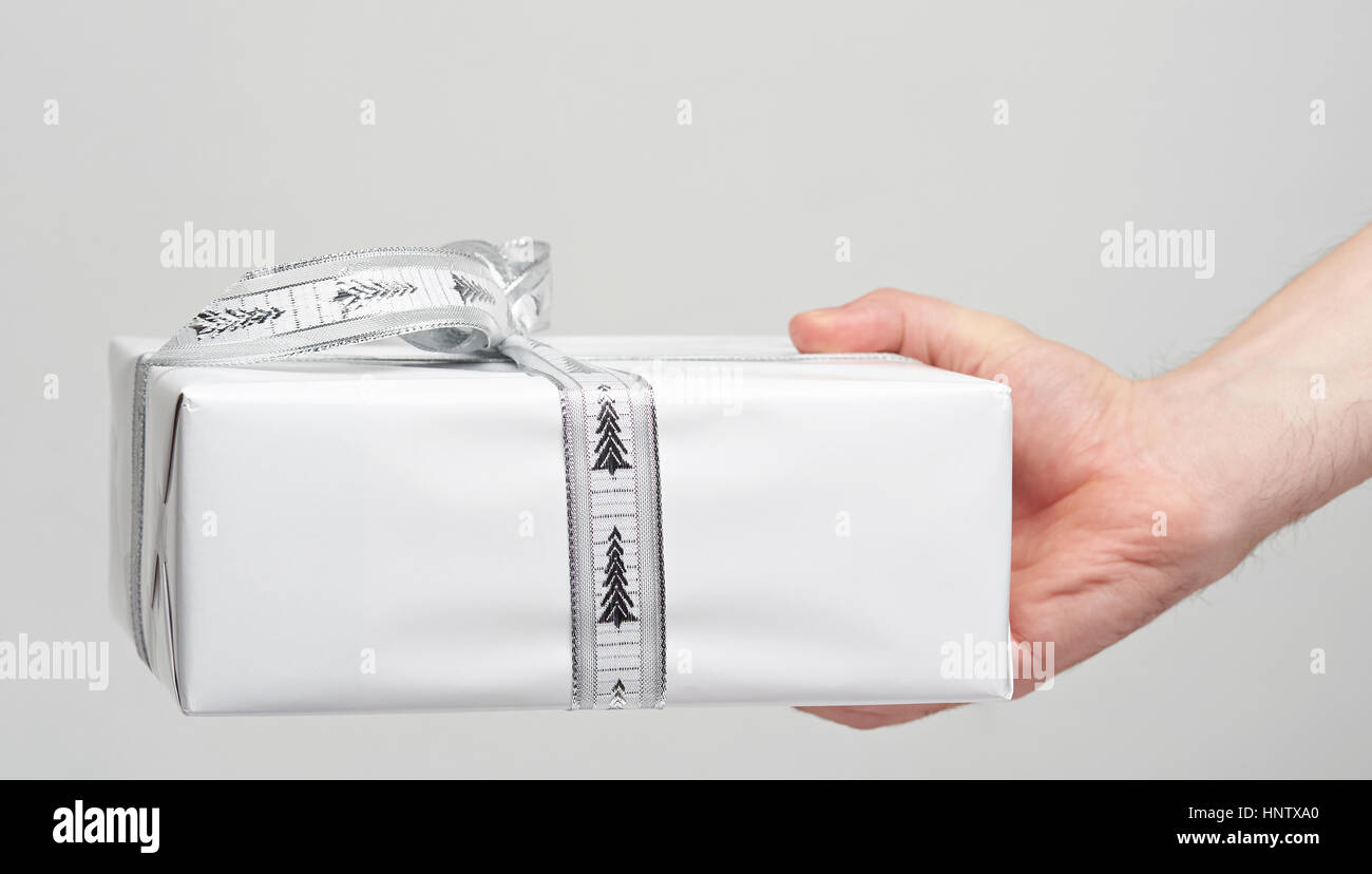Scatola regalo bianca in mano dando con nastro isolato su bianco Foto Stock