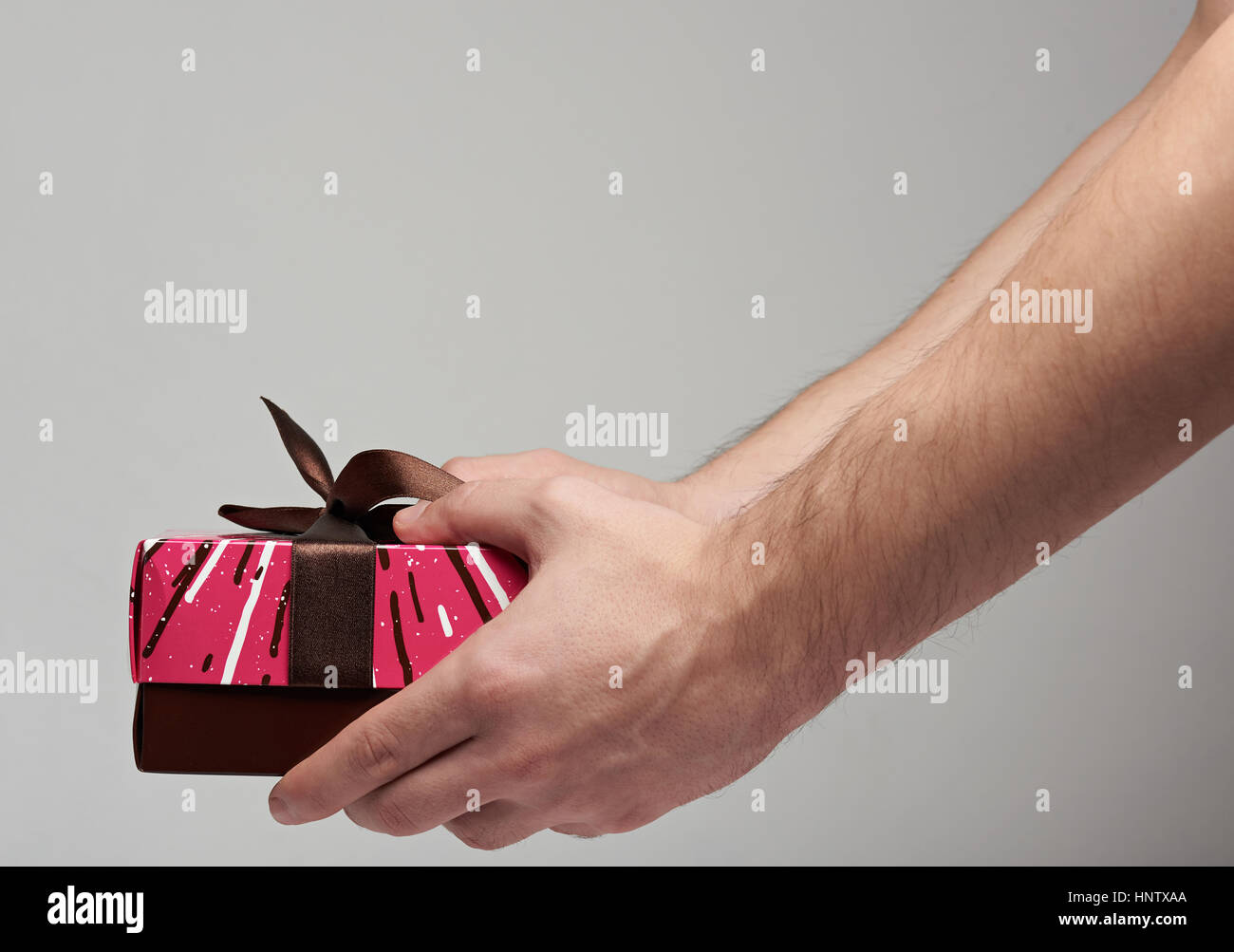 Una coloratissima confezione regalo rossa isolato su sfondo grigio tenendo in mano Foto Stock