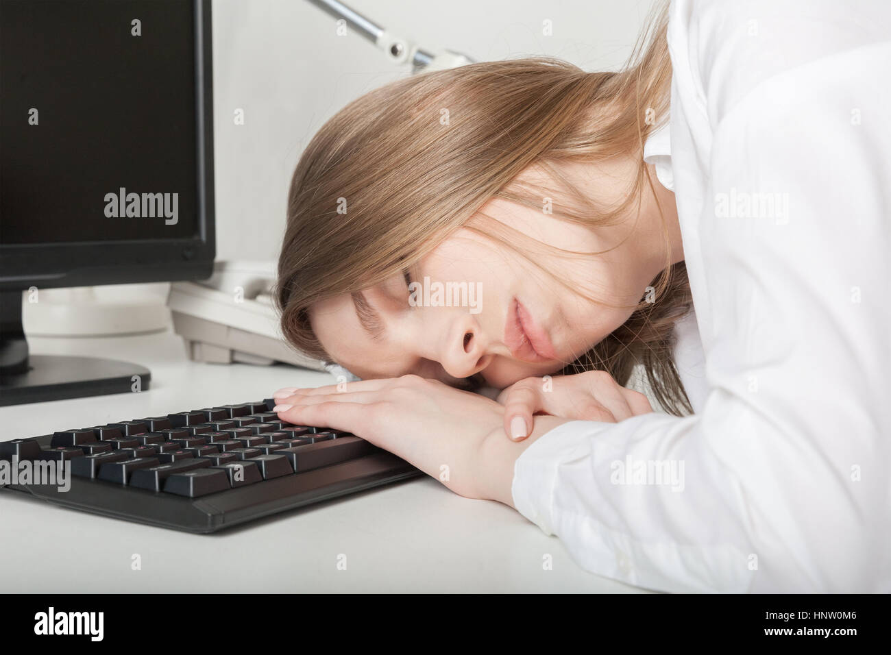 La stanca ragazza dorme in ufficio dietro una scrivania Foto Stock