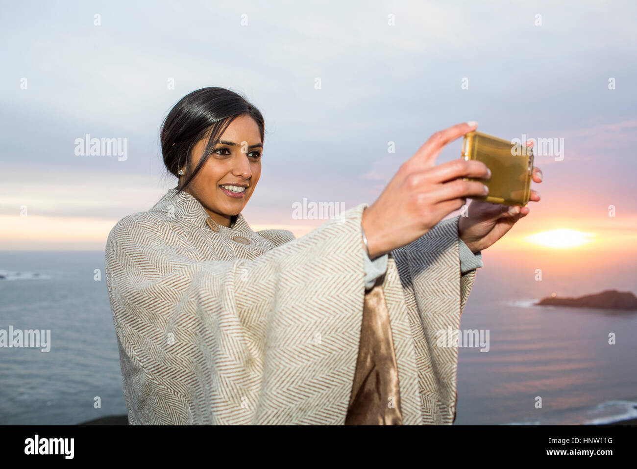 Donna indiana in posa per telefono cellulare selfie vicino oceano Foto Stock