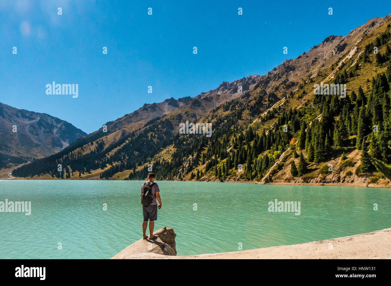 Uomo caucasico permanente sulla roccia vicino al lago di montagna Foto Stock