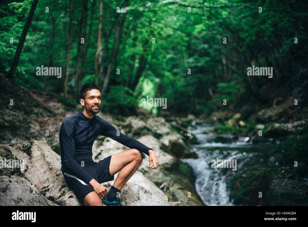 Uomo caucasico seduti sulle rocce vicino al flusso di foresta Foto Stock