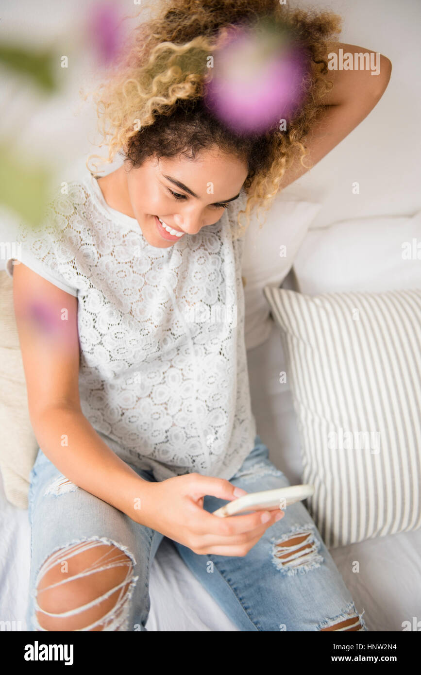 Razza mista donna seduta sul letto gli sms sul cellulare Foto Stock