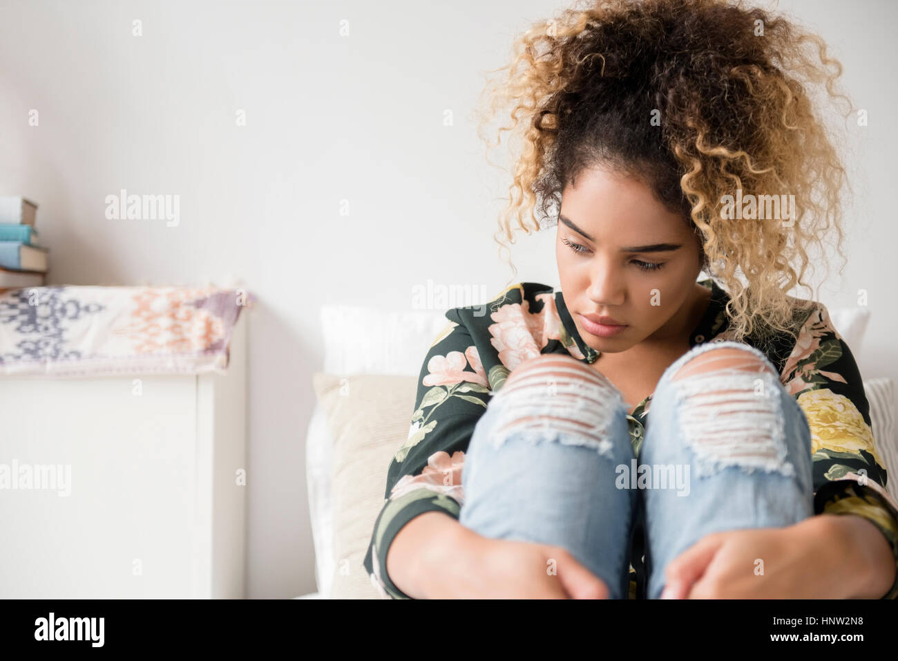Malinconici razza mista donna seduta sul letto Foto Stock