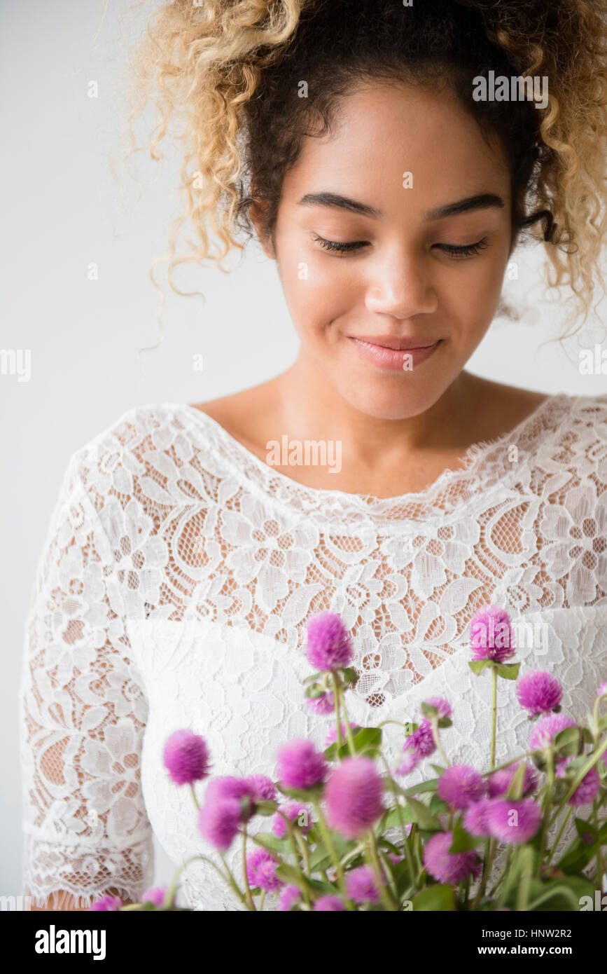 Razza mista donna che indossa abiti da sposa ammirando bouquet Foto Stock