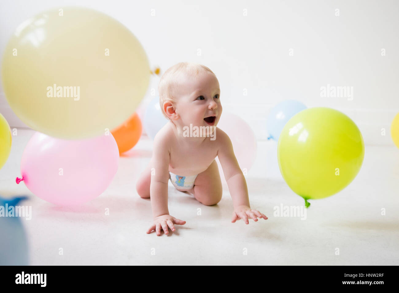 Caucasian baby boy strisciare sul pavimento la visione di palloncini Foto Stock