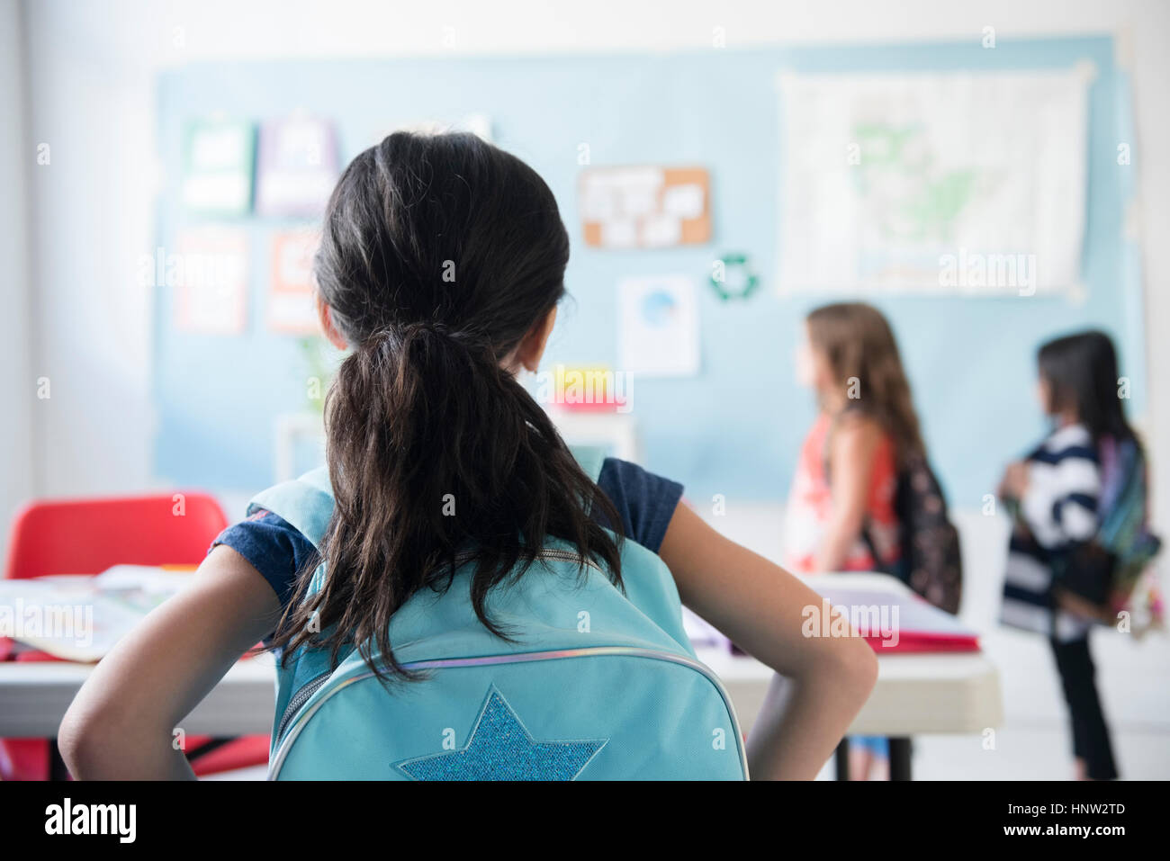 Ragazza in aula indossando uno zaino guardando i compagni di scuola Foto Stock