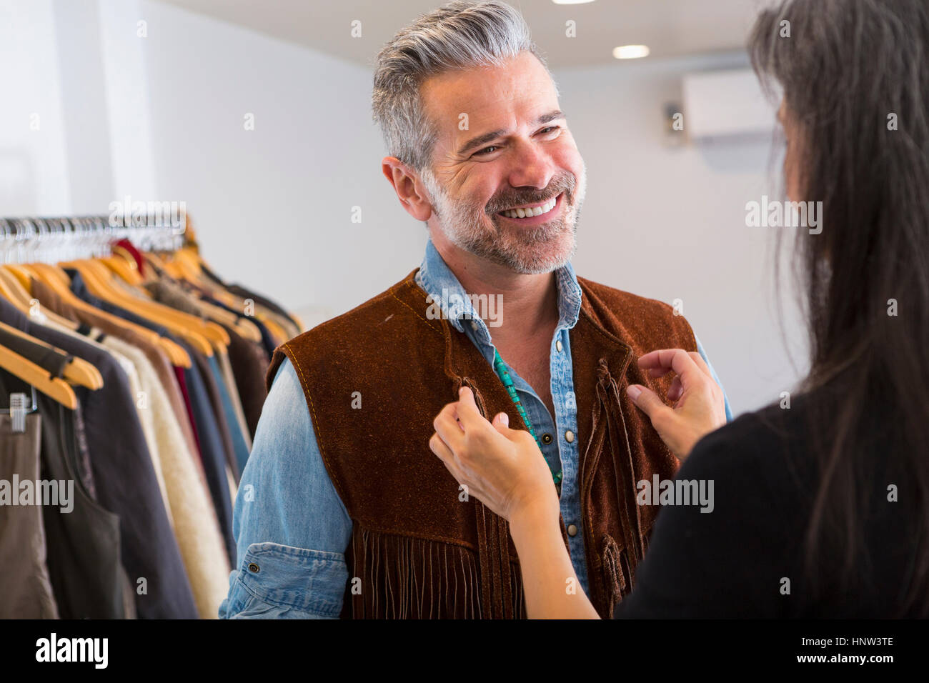 Donna Uomo aiutando con giubbotto di frangia in negozio Foto Stock