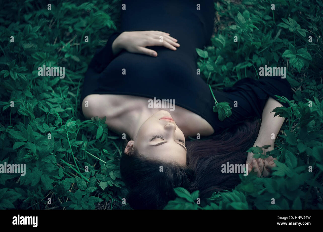 La donna caucasica indossando abiti che stabilisce nel verde fogliame Foto Stock