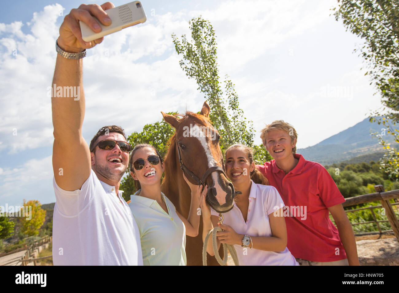 Lo sposo e gli amici prendendo selfie smartphone con cavallo al maneggio rurale Foto Stock