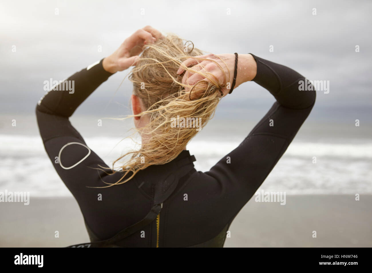 Vista posteriore del surfista femmina bagnato di legatura capelli biondi sulla Rockaway Beach, New York, Stati Uniti d'America Foto Stock