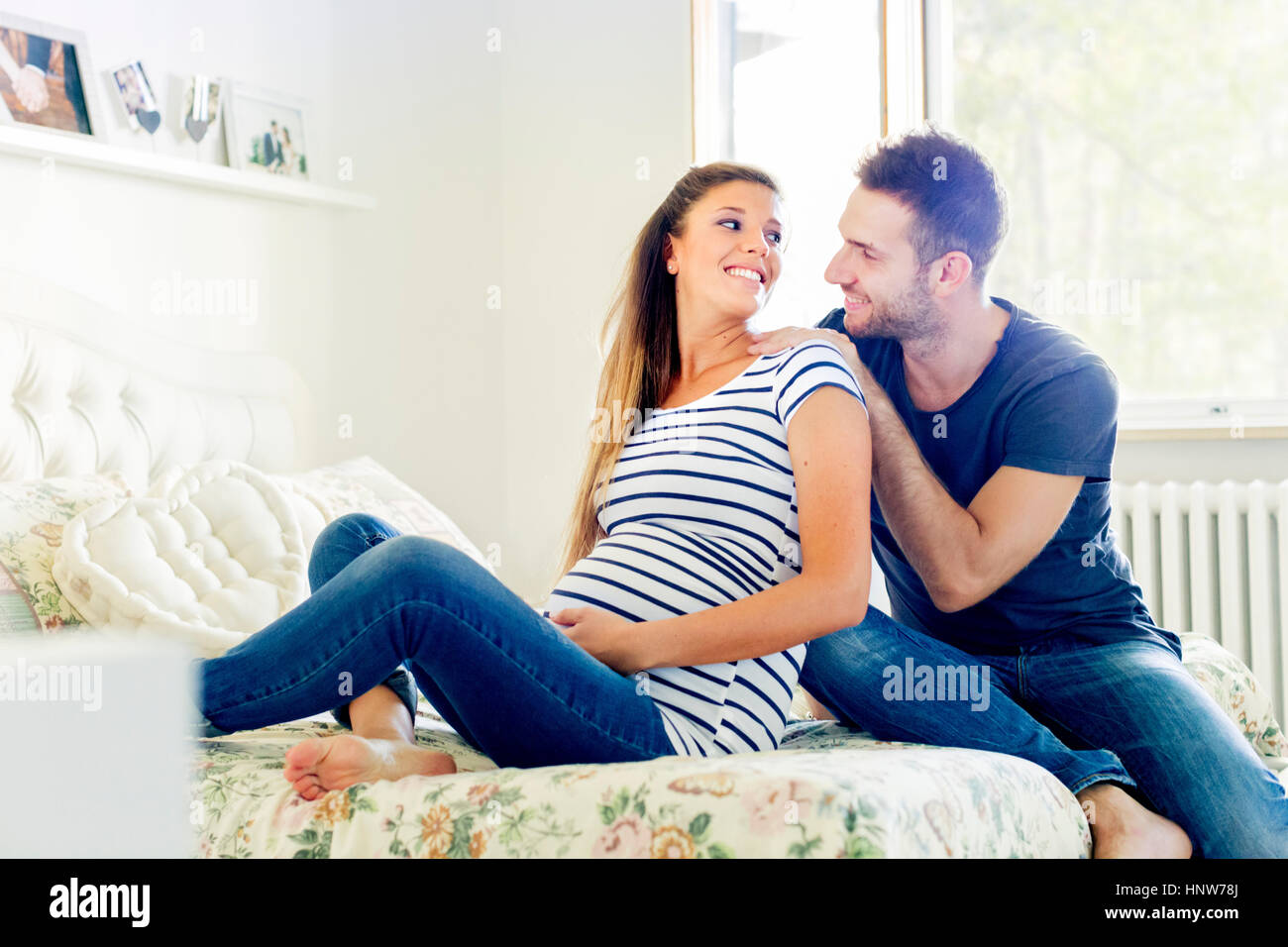 Incinta giovane seduto sul letto sorridente Foto Stock