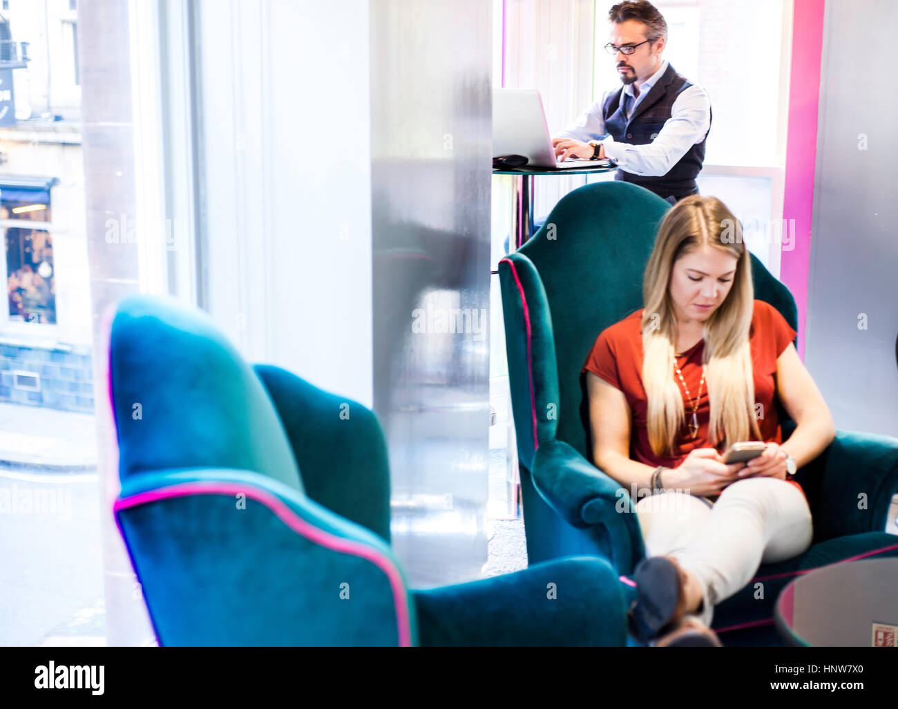 Imprenditore utilizzando portatile mentre client in poltrona da ufficio SMS sullo smartphone Foto Stock