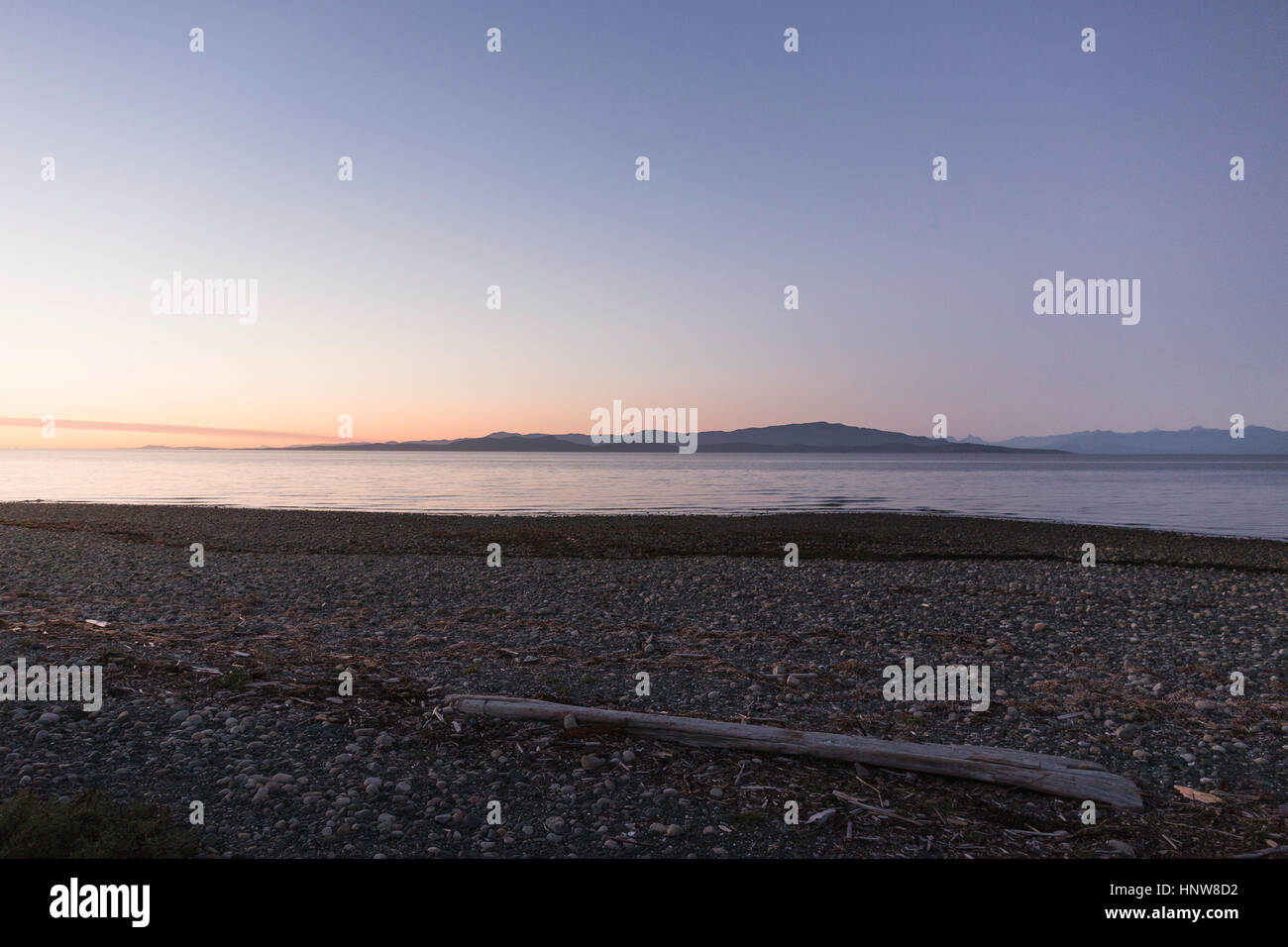 Driftwood log sulla spiaggia al tramonto, Rathrevor Spiaggia Parco Provinciale, Isola di Vancouver, British Columbia, Canada Foto Stock