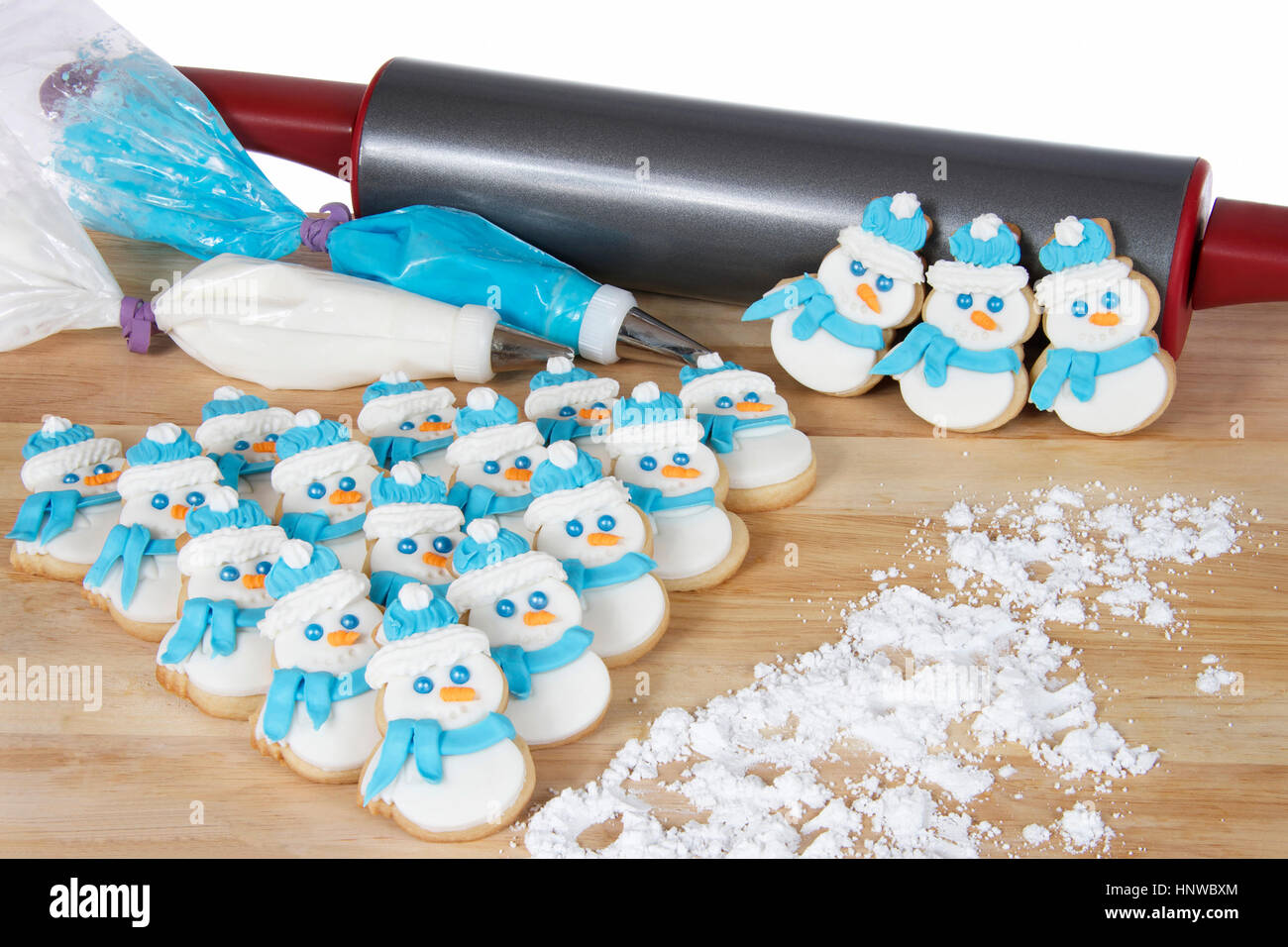 Pupazzi di neve lo zucchero i cookie su una tavola di legno con blu e bianco glassa reale nella decorazione di sacchi con il matterello in background Foto Stock