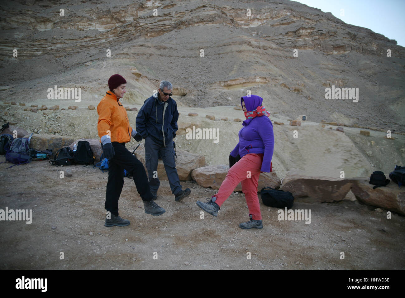 Il congelamento senior citizen escursionisti vestito nella fredda mattina fare tai chi per riscaldarsi prima di iniziare una faticosa escursione. Makhtesh Ramon, Negev, Israele. Foto Stock