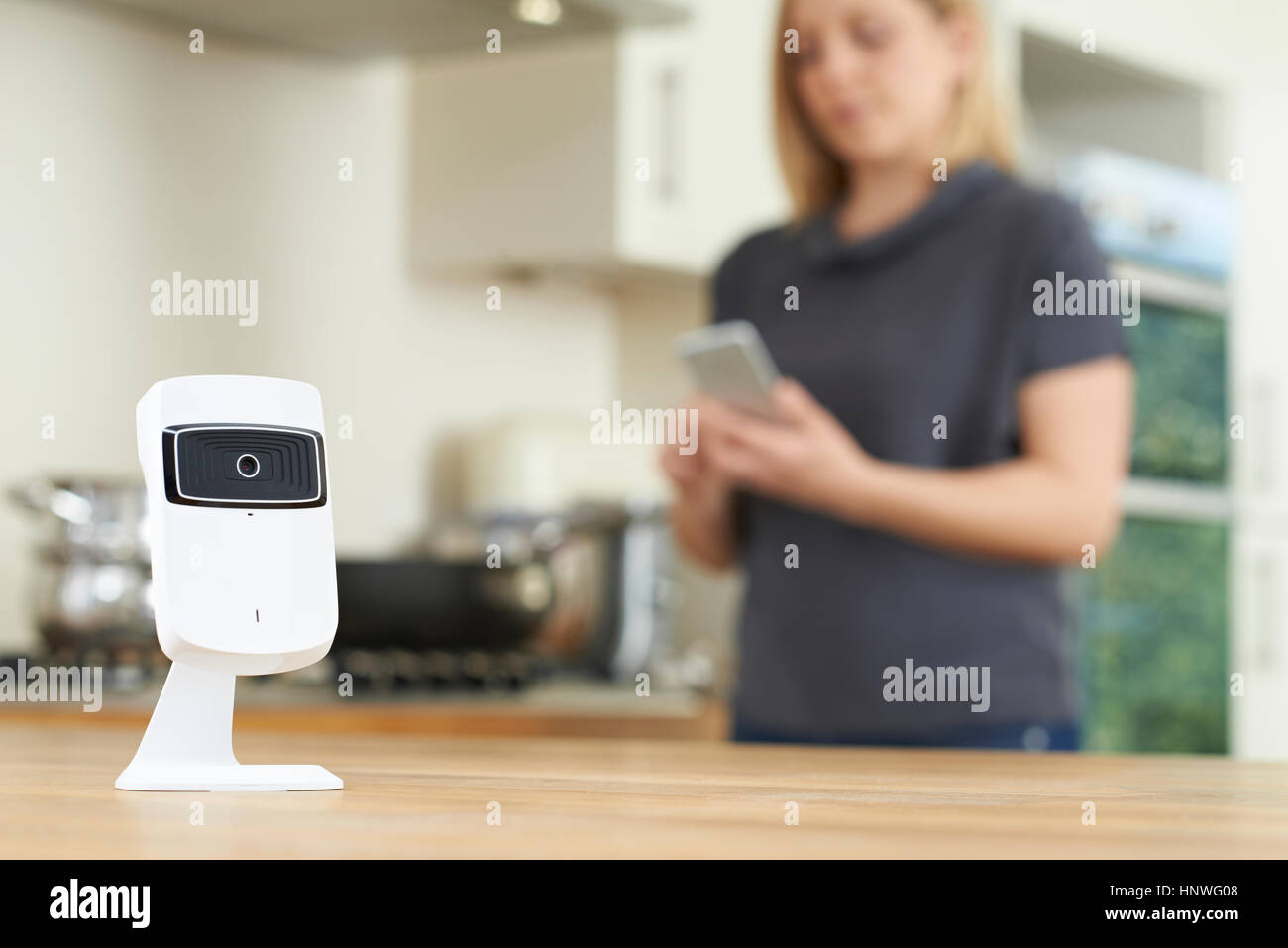 La donna il controllo Smart videocamera di sicurezza utilizzando l'App sul telefono cellulare Foto Stock