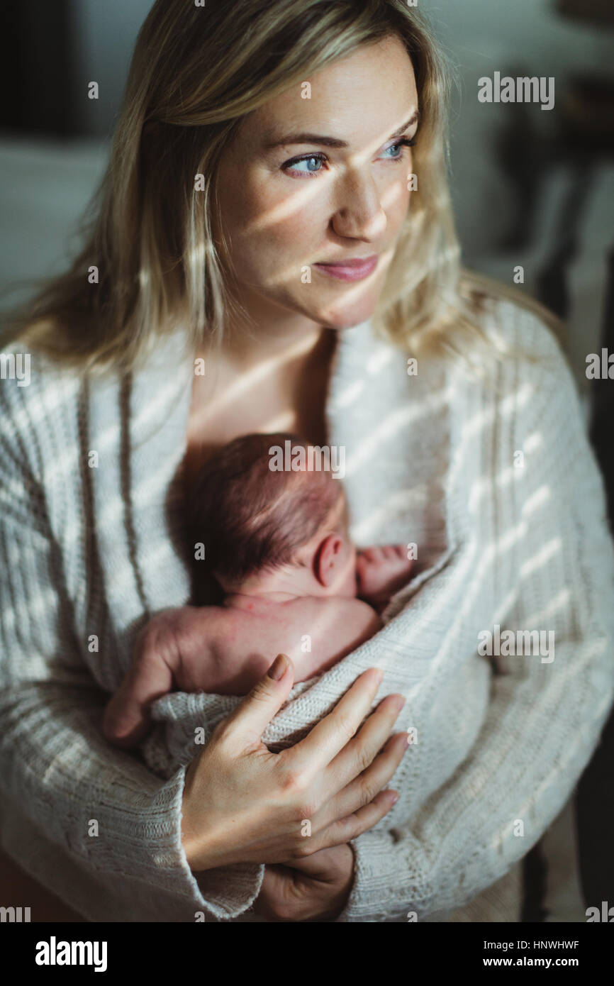 Ritratto di metà donna adulta cullano new born baby figlia avvolto in cardigan Foto Stock