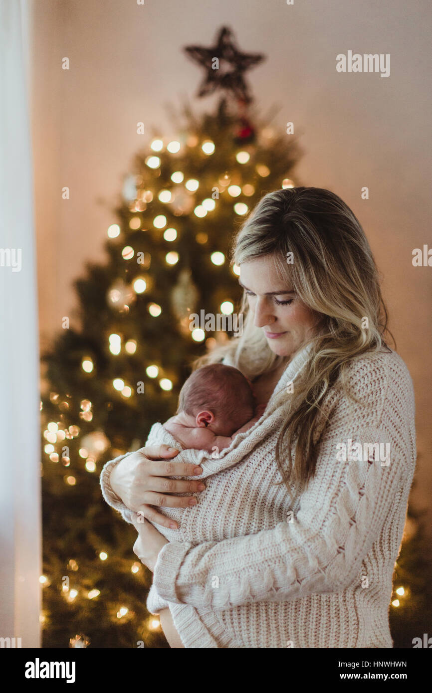 Metà donna adulta cullano new born baby figlia avvolto in cardigan a Natale Foto Stock