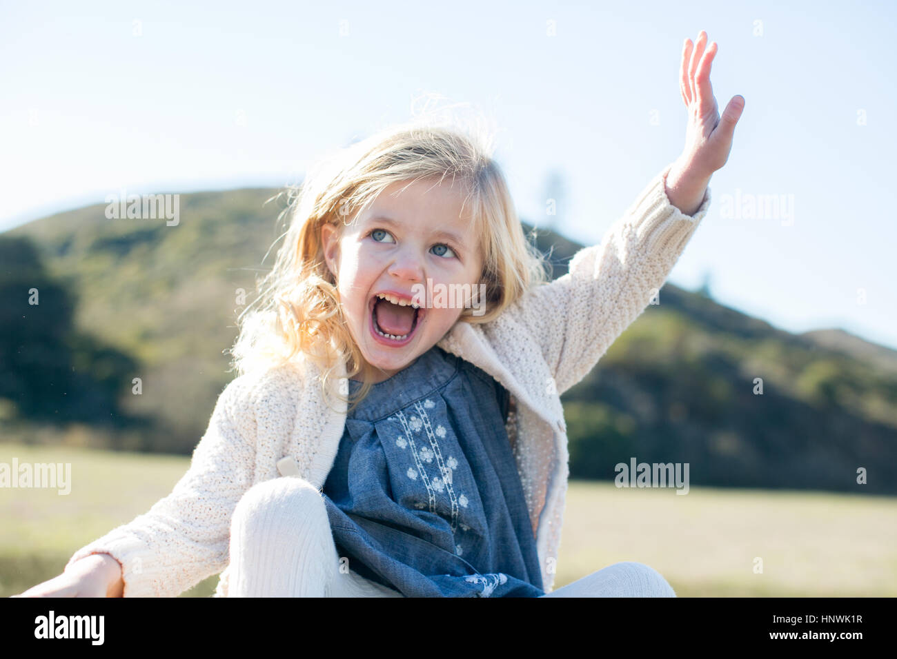 Carina ragazza bionda seduta sventolare nel paesaggio di campo Foto Stock