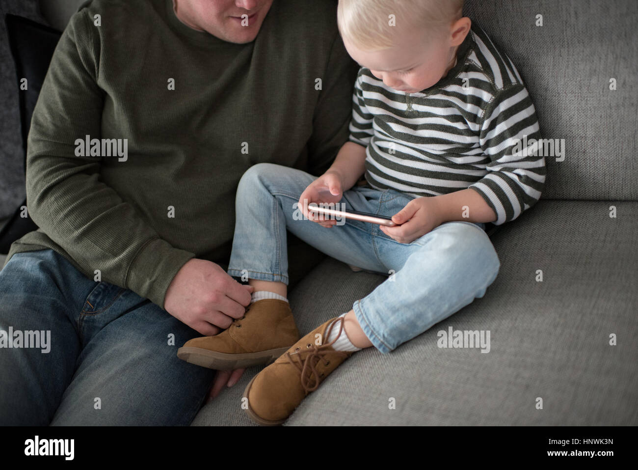 Padre e figlio seduti sul divano, figlio guardando smartphone Foto Stock