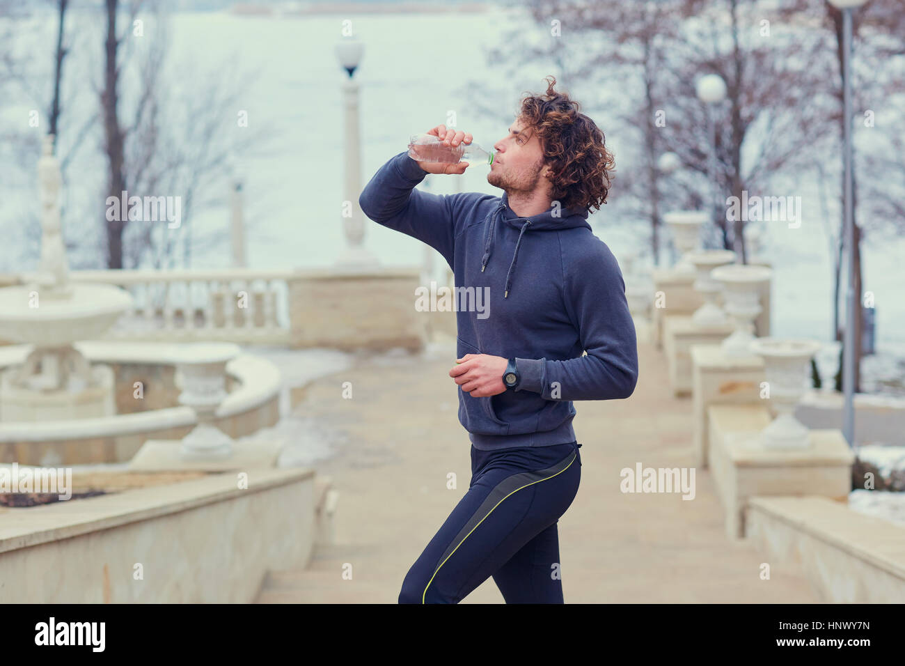 Ricci runner maschio beve l'acqua da una bottiglia in posizione di parcheggio sul stai Foto Stock