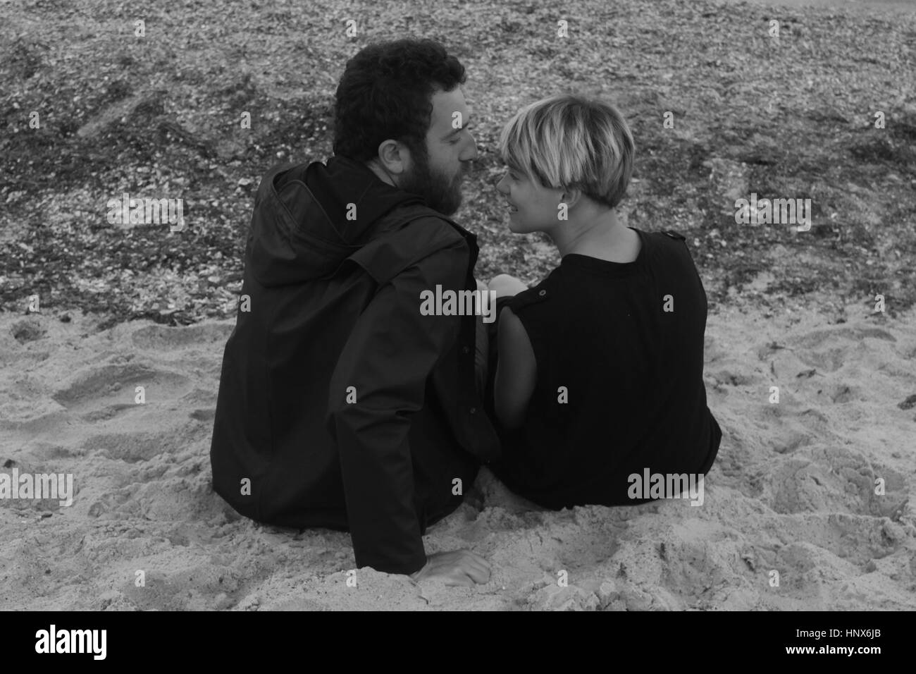 Coppia giovane seduto sulla spiaggia, faccia a faccia vista posteriore Foto Stock