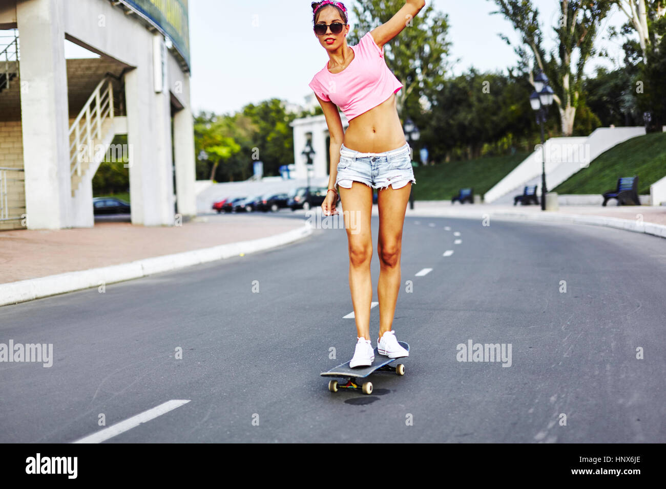 Giovane donna lo skateboard lungo la strada Foto Stock