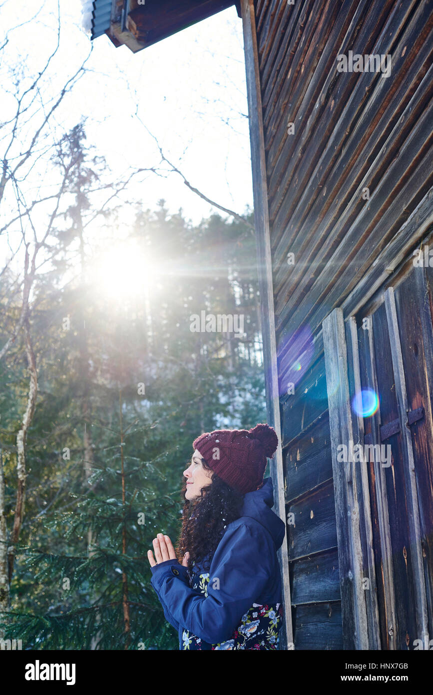 Donna in knit hat a praticare yoga e meditazione da log cabin Foto Stock