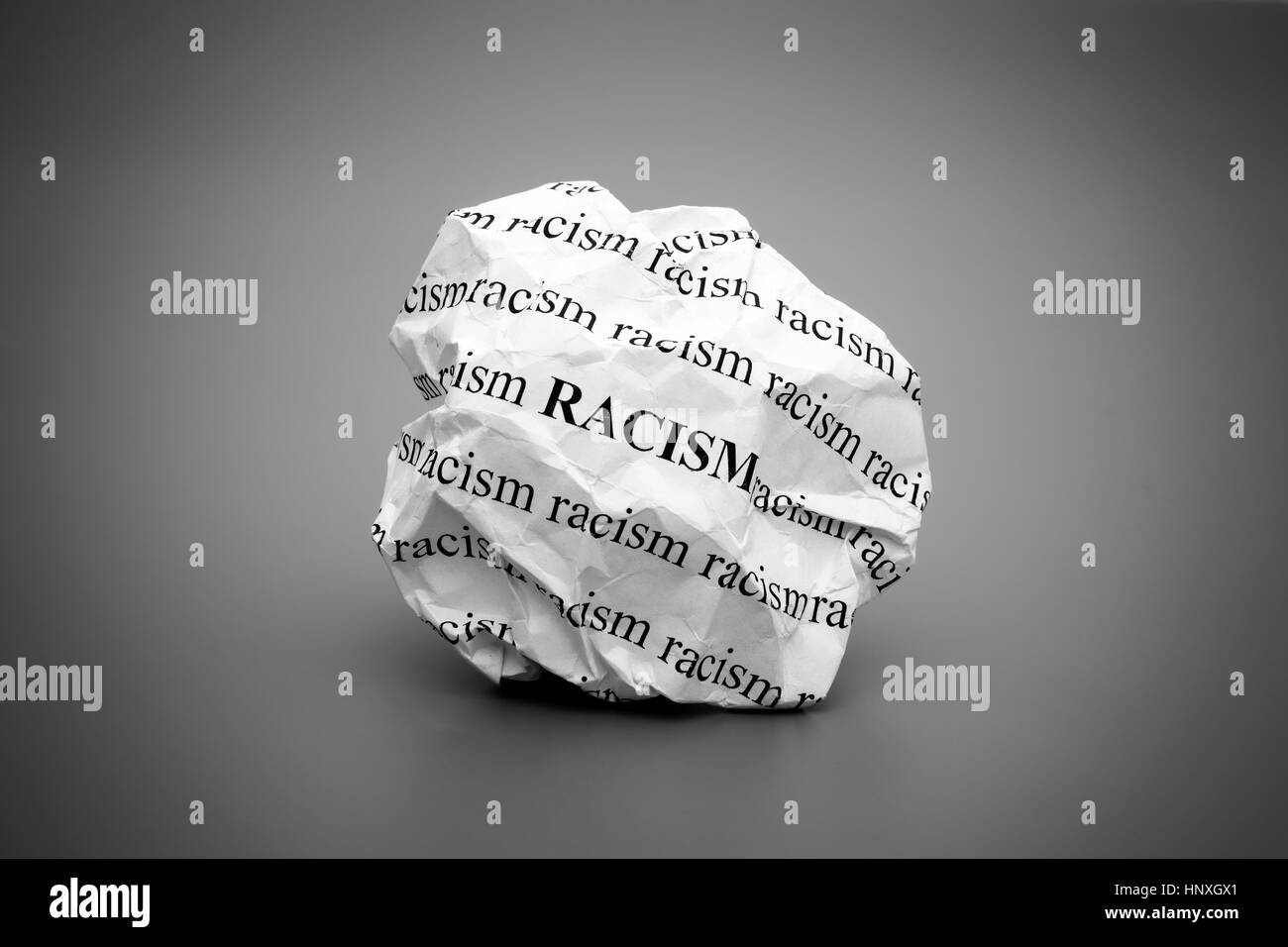 Carta sgualcita sfera con parole il razzismo su sfondo grigio. In bianco e nero. Foto Stock