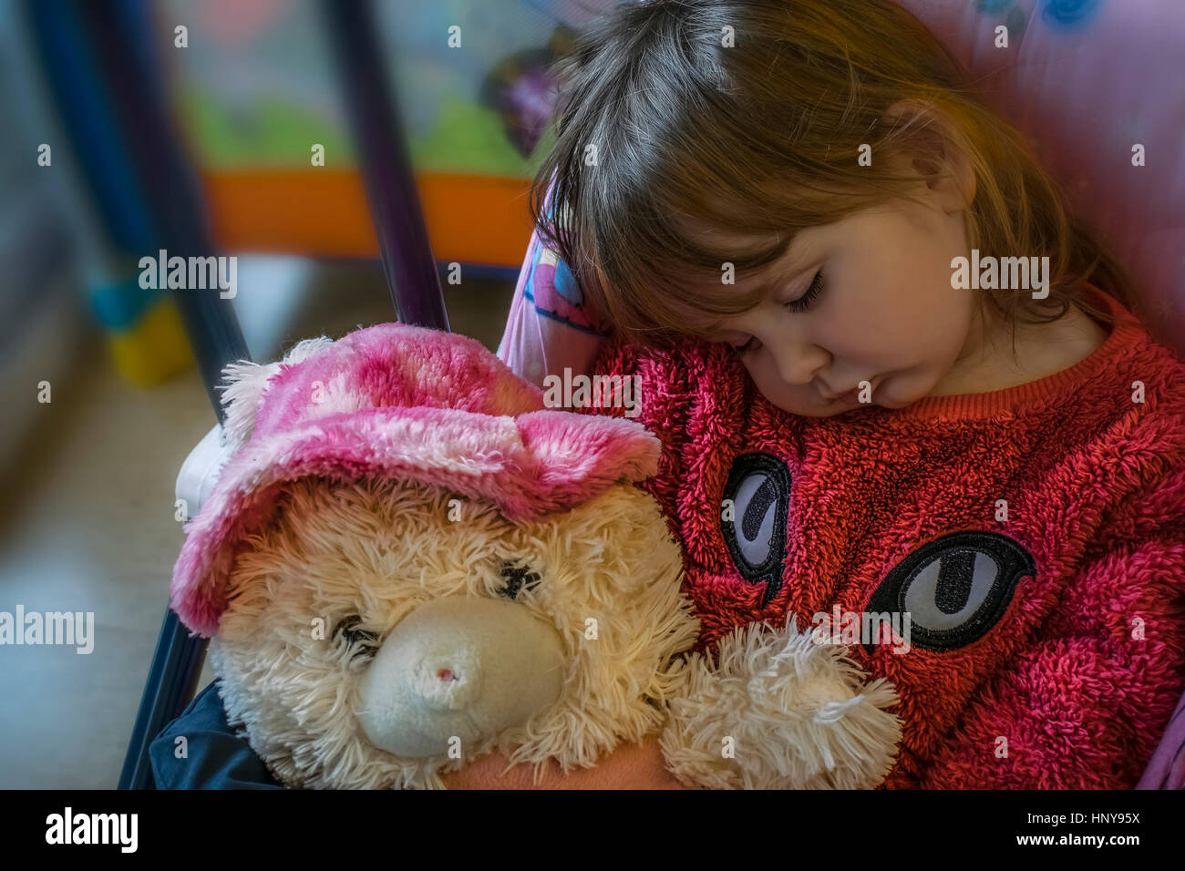 Blonde baby ragazza seduta sul baby swing, addormentato tenendo una pelliccia Teddy bear. Indossa una pelliccia rosa maglione. Foto Stock