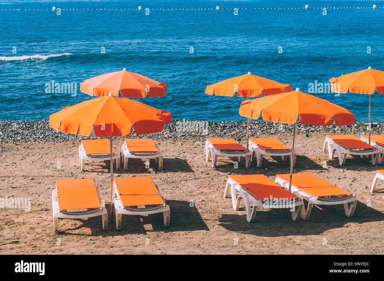 Arancione di ombrelloni e sdraio contro la spiaggia di ghiaie e oceano Foto Stock