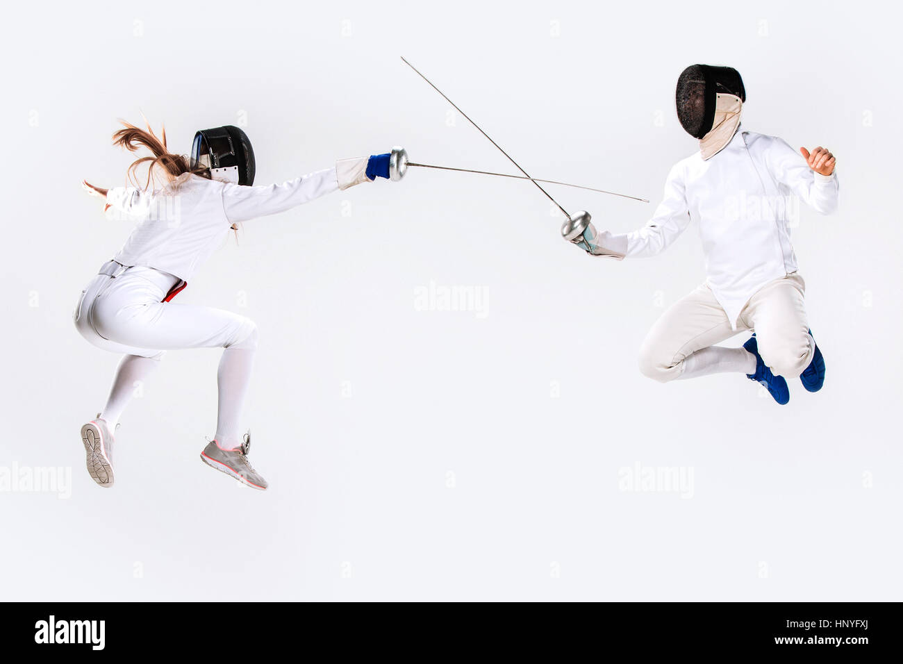 La donna e l uomo indossare tuta scherma la pratica con la spada contro il grigio Foto Stock
