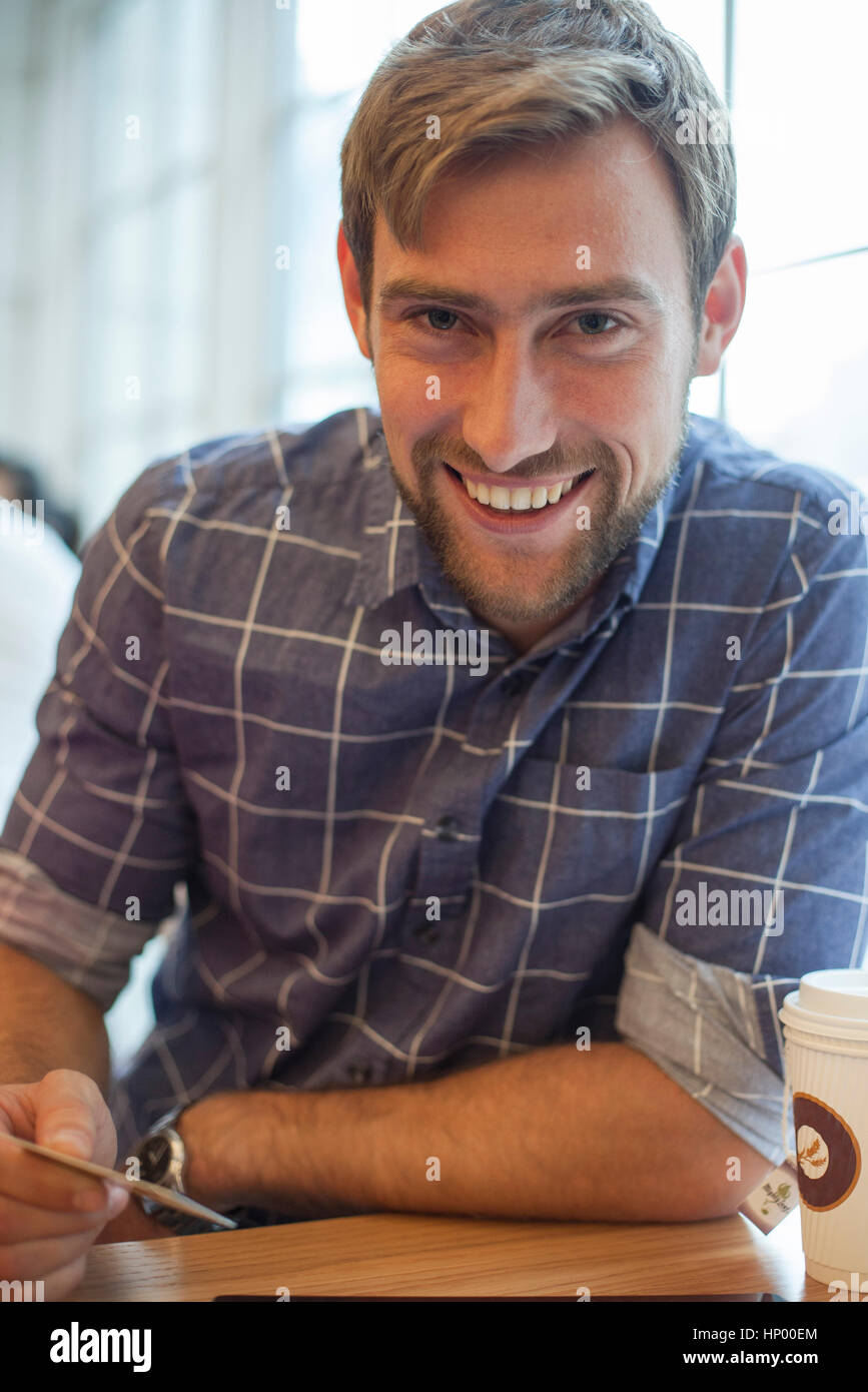 Uomo seduto in un coffee shop con la carta di credito in mano, sorridente allegramente Foto Stock