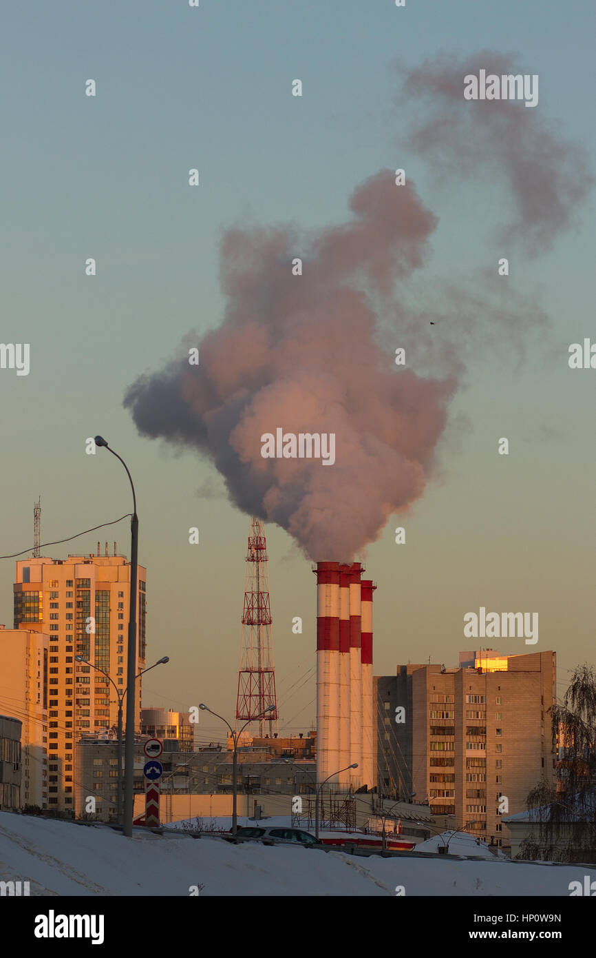 Il fumo delle ciminiere nella luce del tramonto sullo sfondo della città Foto Stock