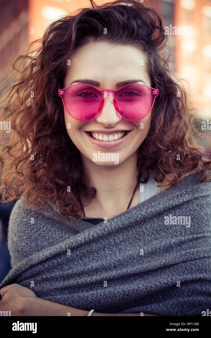 Donna che indossa gli occhiali da sole rosa, sorridente allegramente, ritratto Foto Stock