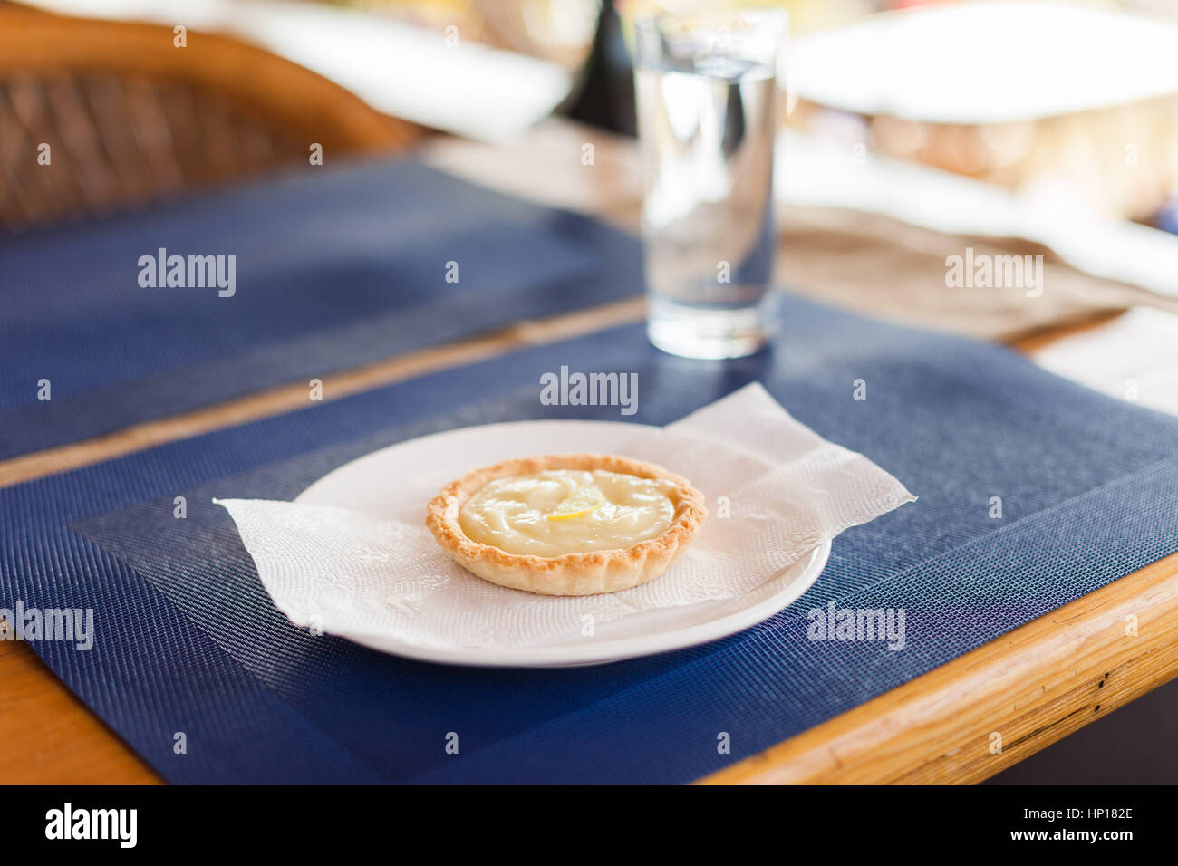 Crostata al limone con crema pasticcera riempimento e le fette di limone su una piastra bianca, blu opaco, e legno cafe tabella Foto Stock