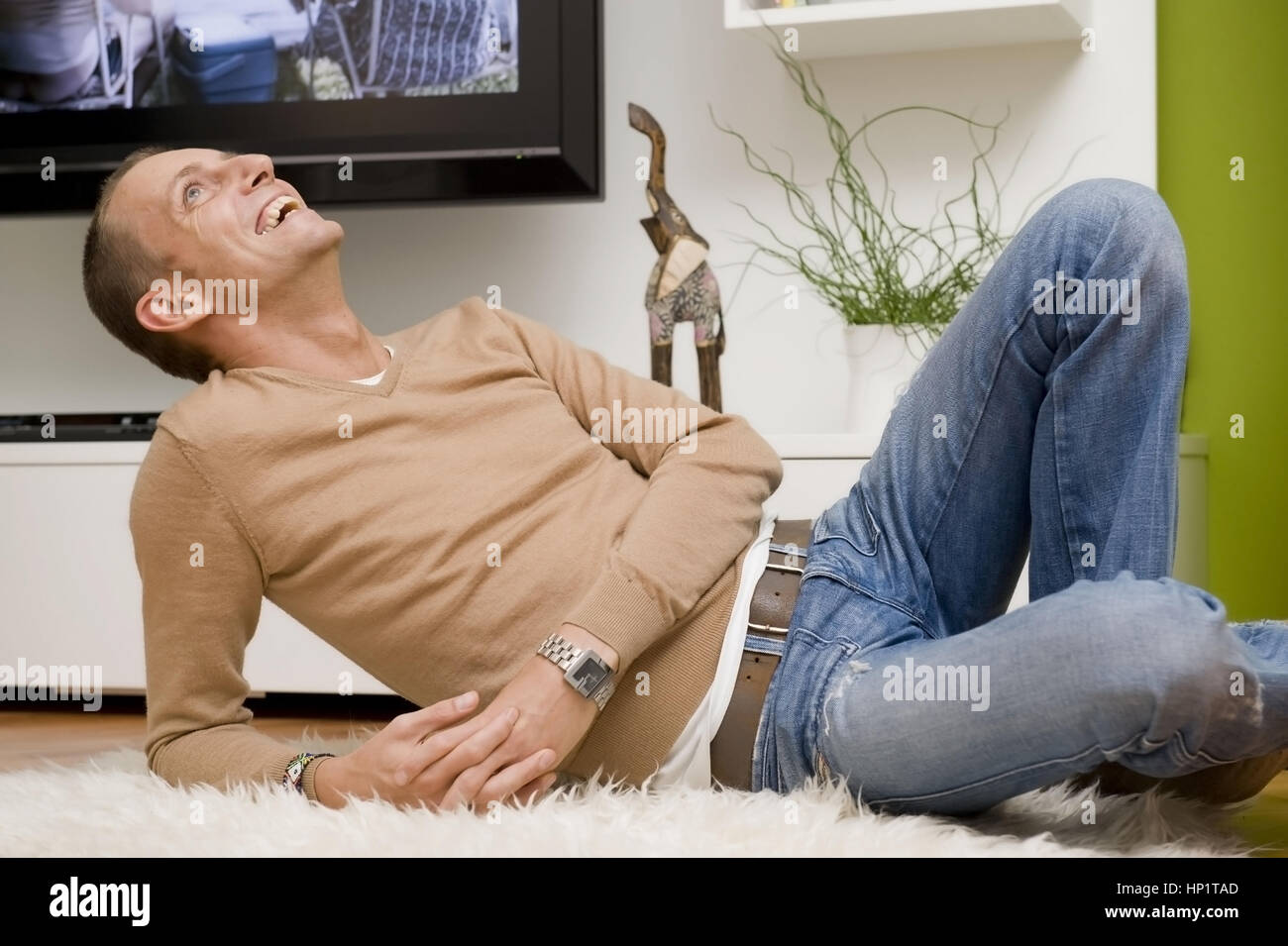 Modello di rilascio , Junger Mann 30+, liegt gemuetlich auf Schafsfell am Fussboden - giovane in un momento di relax a casa Foto Stock