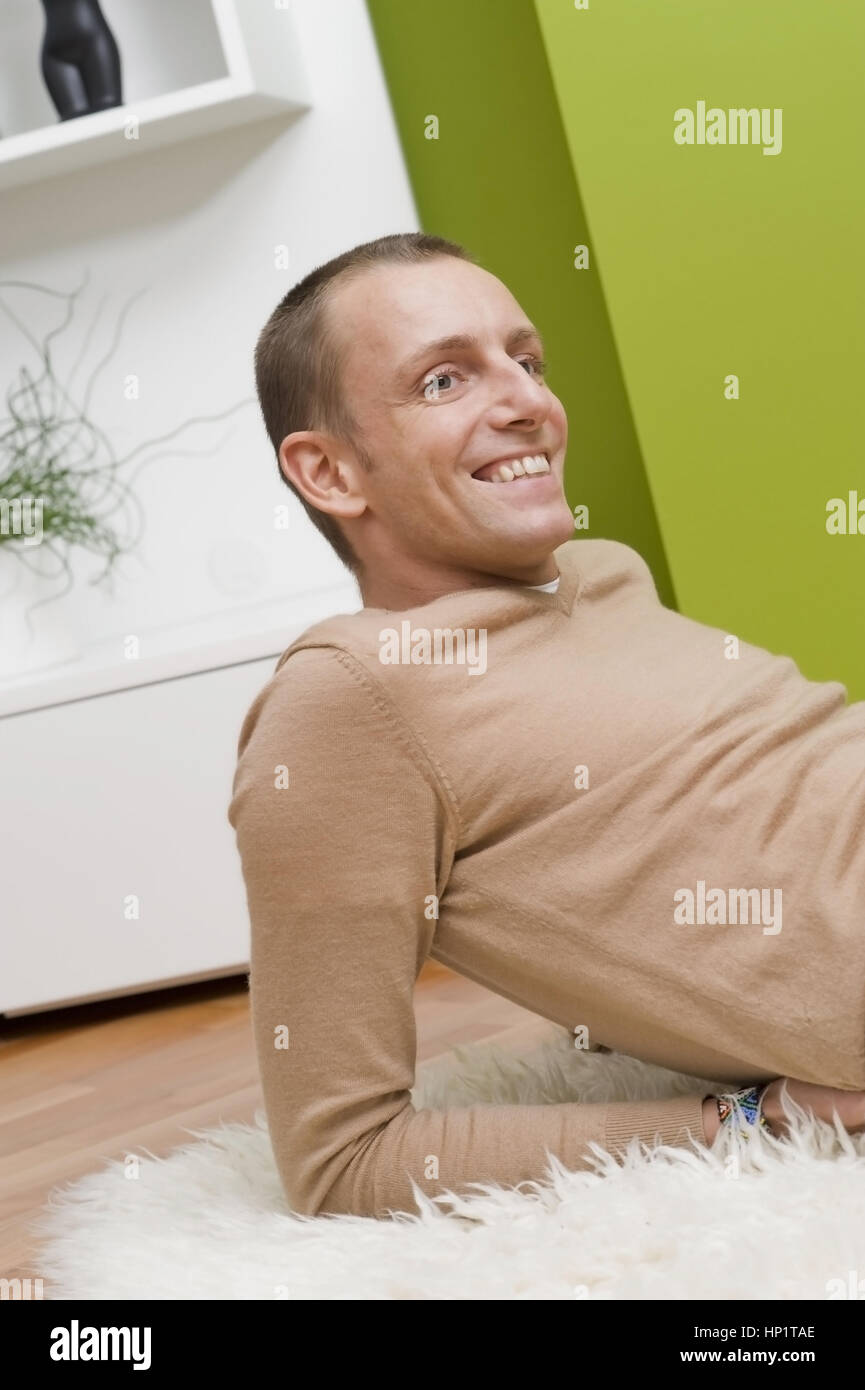 Modello di rilascio , Junger Mann 30+, liegt gemuetlich auf Schafsfell am Fussboden - giovane in un momento di relax a casa Foto Stock