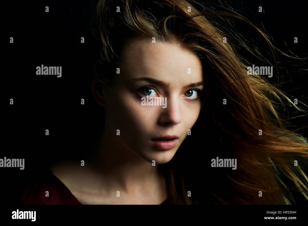 Bella ragazza guarda gli occhi di perforazione nella fotocamera. Capelli battenti. Dramma. Studio fotografico in chiave di basso su sfondo scuro Foto Stock