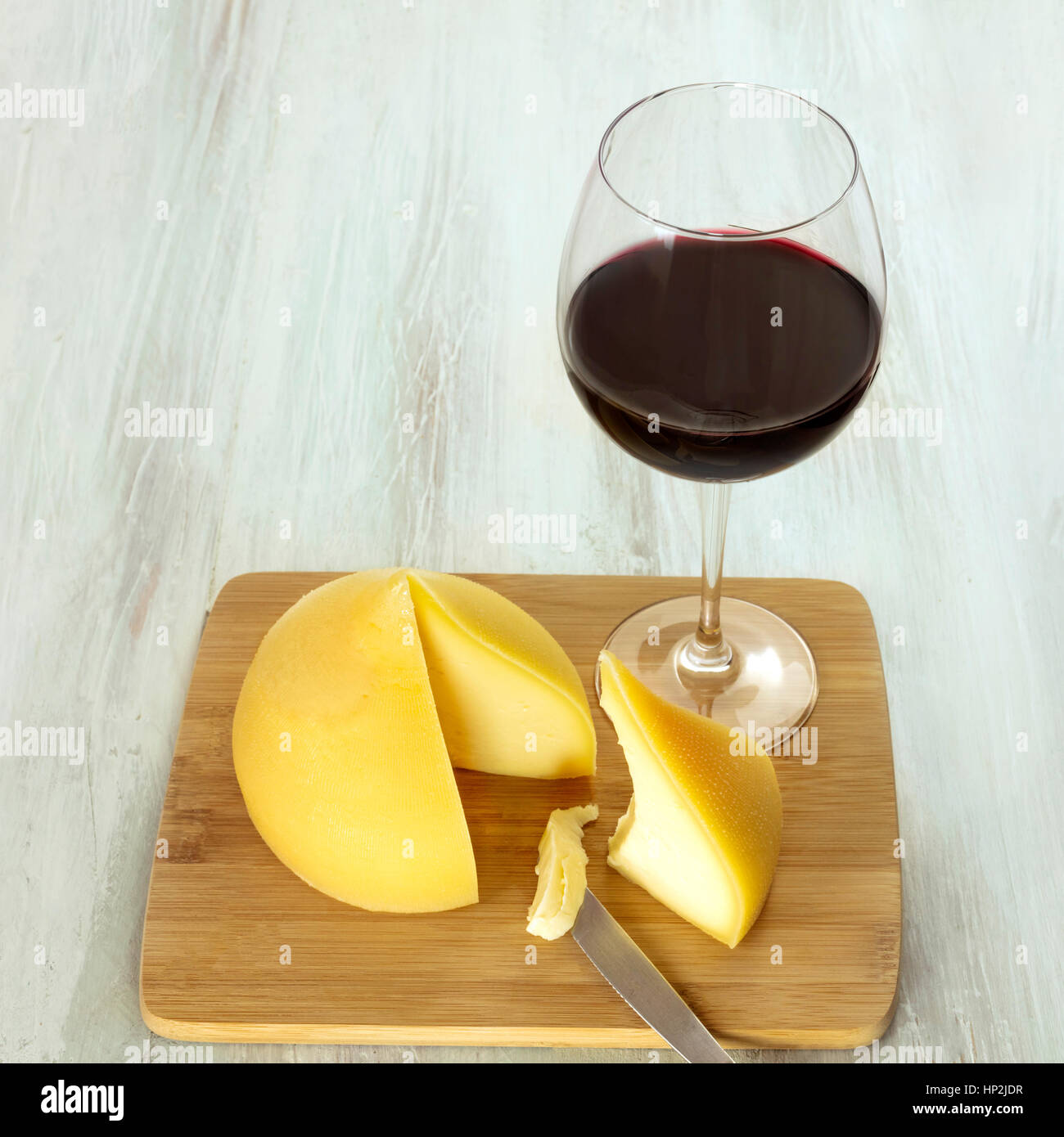 Una foto di tetilla, un tradizionale spagnolo soft formaggio di latte di  vacca, con una fetta tagliata e un bicchiere di vino rosso, su una tavola  di legno con un posto per