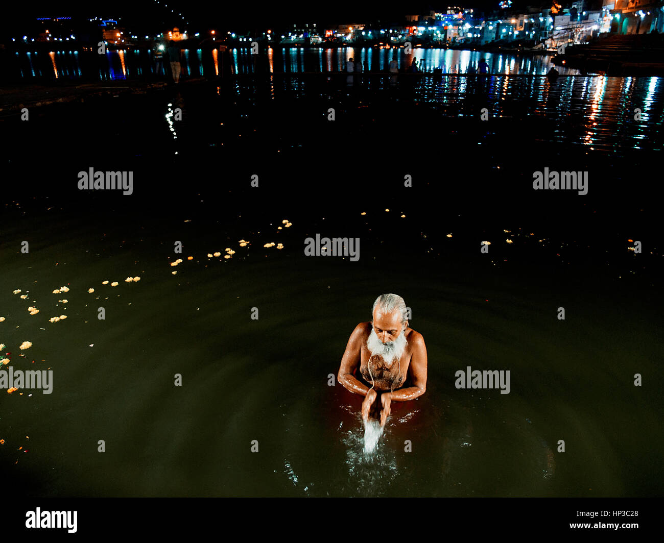 Un sadhu metà immerso nell'acqua, piega le mani nel Lago di Pushkar durante la notte, l'acqua e le spie del ghats visibile Foto Stock