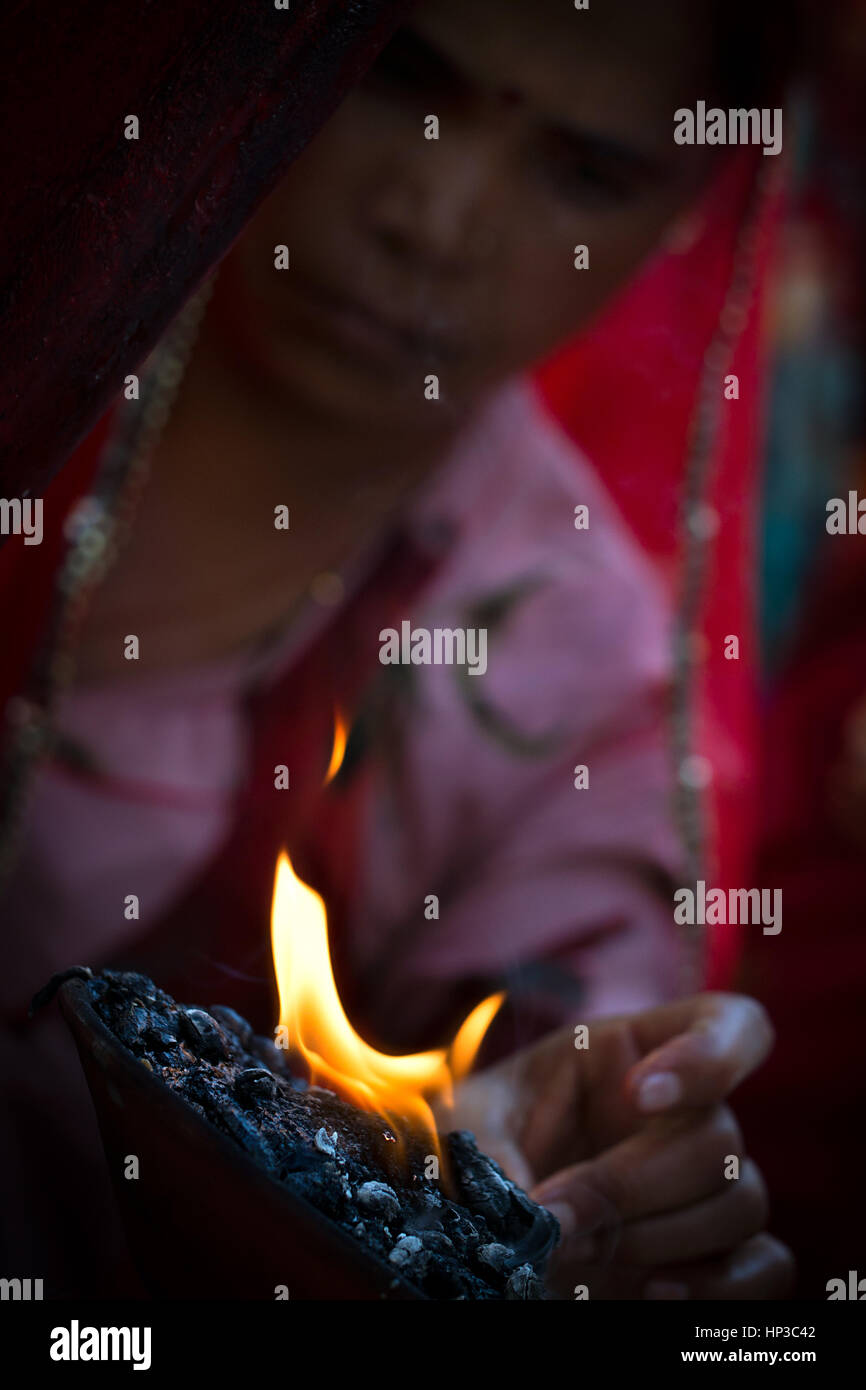 Una donna indiana, indossando il tradizionale rosso e rosa vestiti, toccando il fuoco santo Foto Stock