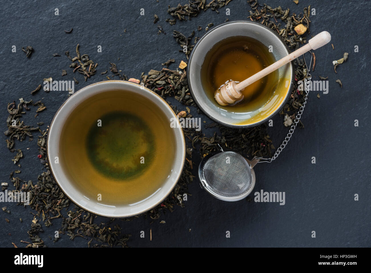 Una tazza di tè e un vaso di miele su uno sfondo nero. Accanto al campo di bocce sono le foglie di tè e di un set per la preparazione di tè infusore. Foto Stock
