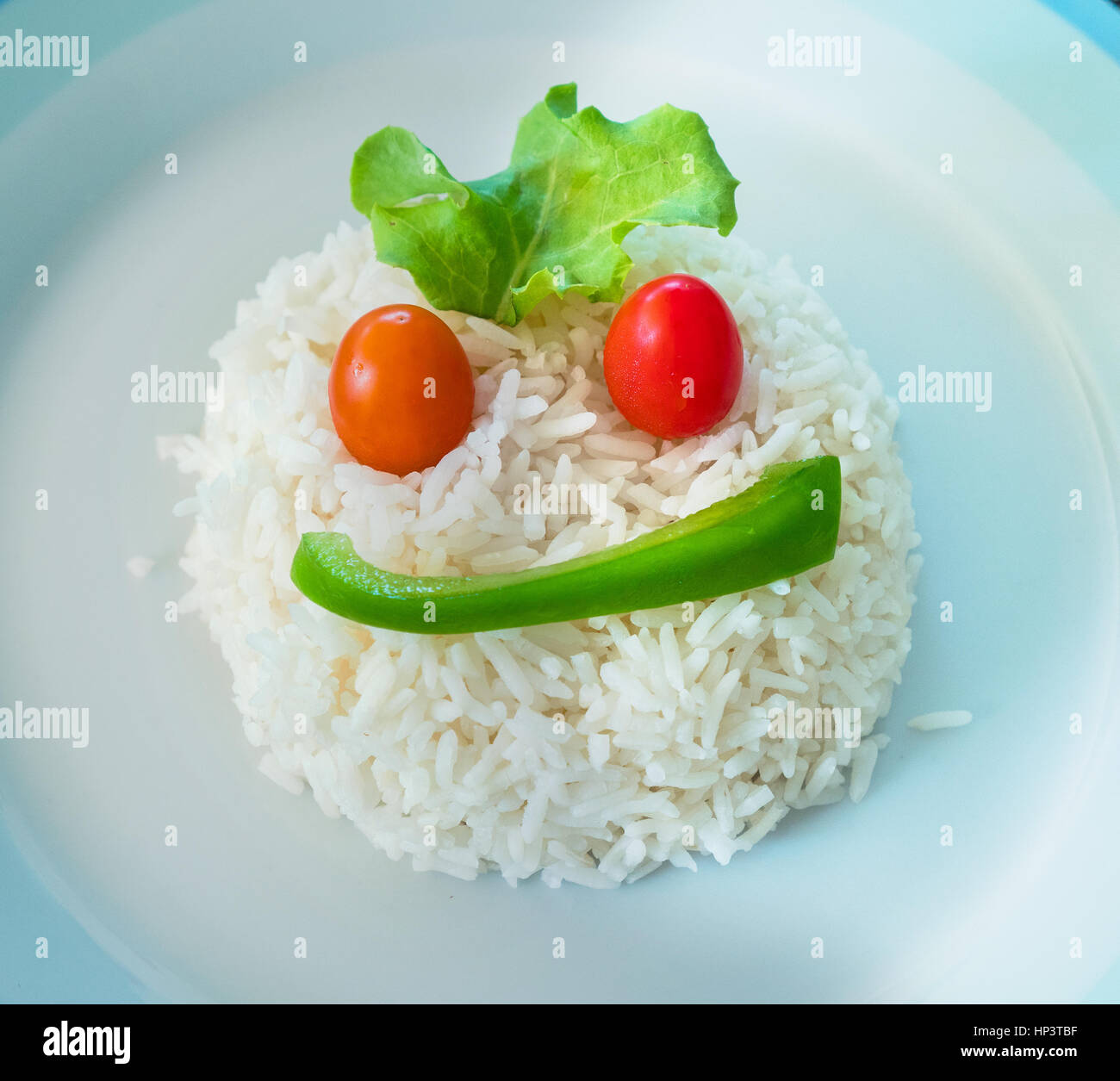Una porzione di riso in bianco su una piastra sagomata come una faccia con  una fetta di peperone verde, due pomodori ciliegia e una foglia di insalata  Foto stock - Alamy