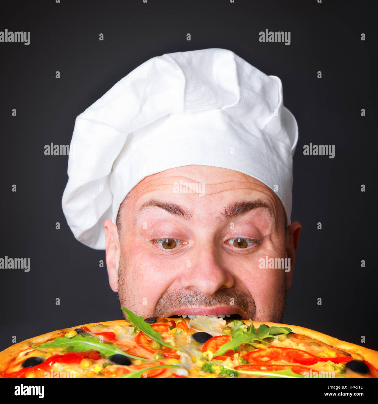 Ritratto di felice attraente cook con una pizza in studio un sfondo nero Foto Stock