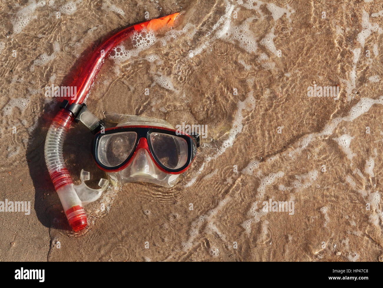 Maschera e snorkel giacente sulla sabbia bagnata con onde. Foto Stock