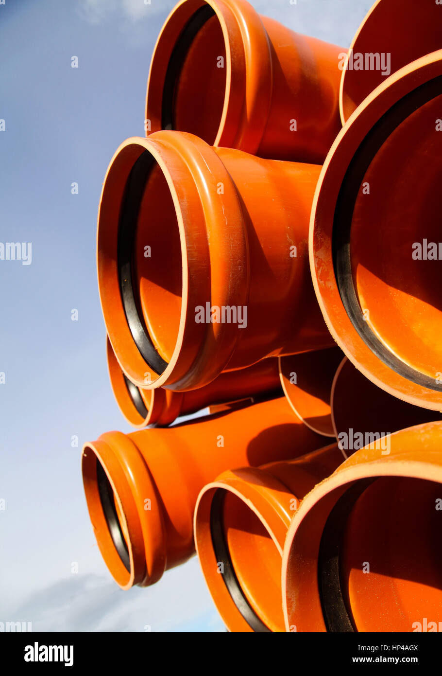 Orange tubi di plastica nella pila in attesa di essere collocate nel sistema fognario, e vi è il cielo blu troppo! Foto Stock
