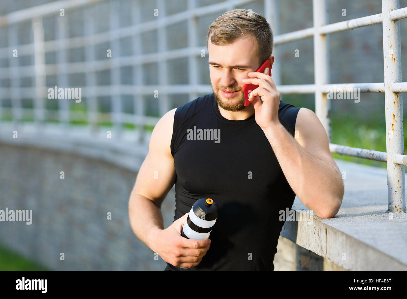 Uomo che parla al telefono e tenendo la bottiglia con acqua Foto Stock
