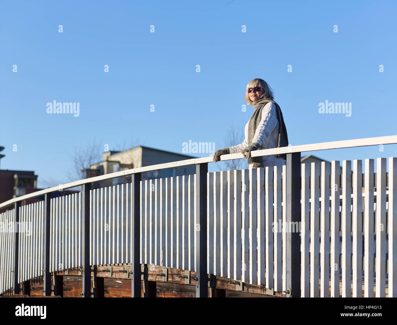 Donna matura appoggiata contro il corrimano del ponte, soleggiata giornata invernale Foto Stock